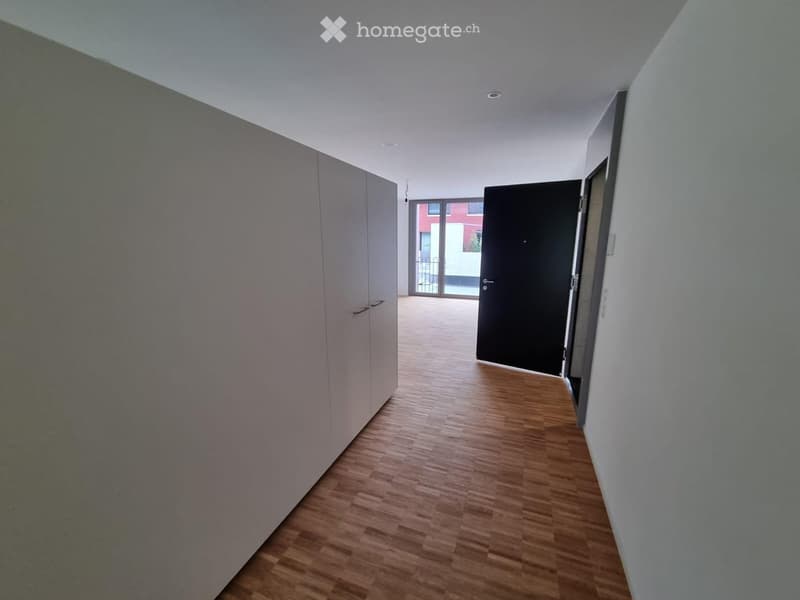 Empty hallway with wooden flooring, white walls, and a door leading to another room.