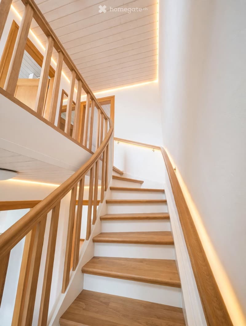 Spiral staircase with wooden steps and handrails, white walls, and recessed lighting.