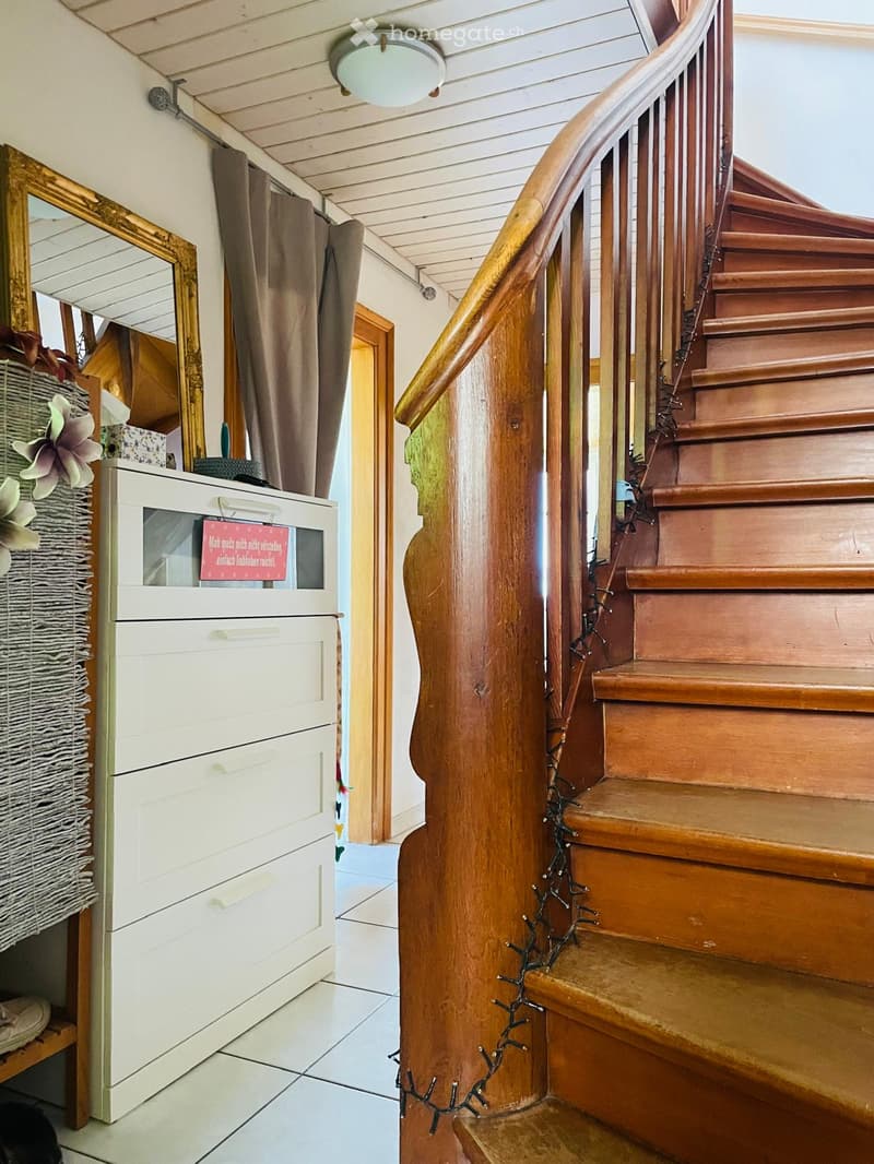 Spiral staircase with wooden steps and handrail, white cabinet with drawers, mirror, and decorative items on a shelf.