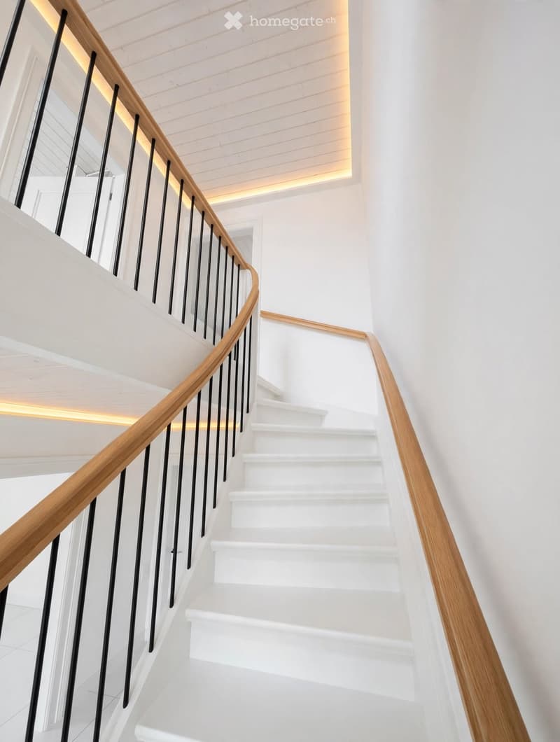 Modern staircase with white steps, wooden handrail, and black balusters, illuminated by warm lighting.