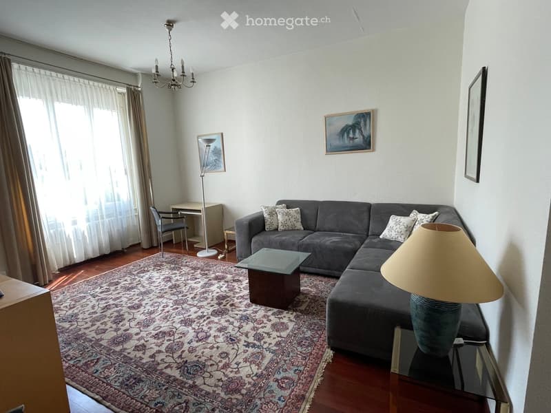 Modern living room with a grey sectional sofa, glass coffee table, floor lamp, side table, and artwork on the walls.
