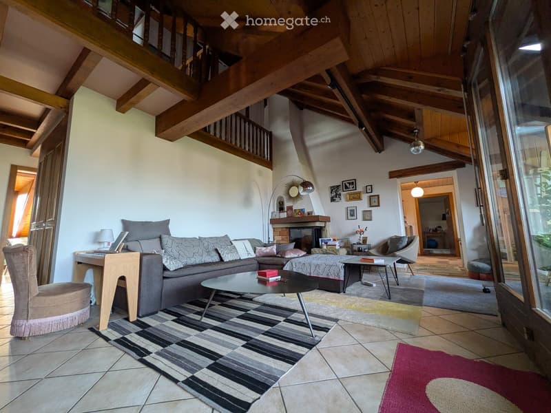 Living room with exposed wooden beams, a grey sectional sofa, coffee table, fireplace, and a large window with a view.