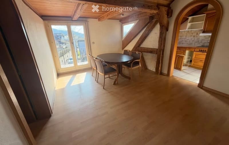 Bright dining area with wooden floor, exposed wooden beams, large windows offering a scenic mountain view, and a round dining table with chairs.