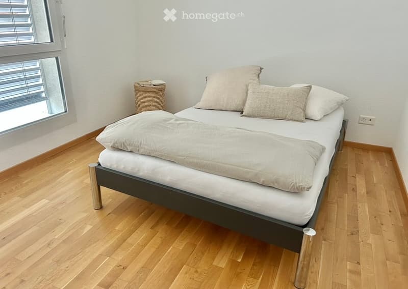 Cozy bedroom with a neatly made bed, pillows, and a wicker basket near the window.