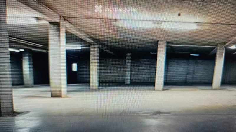 Empty room with bare walls and a concrete floor, featuring several large, dark windows and structural columns.
