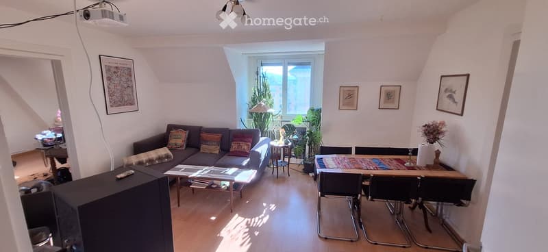 Bright living room with wooden flooring, large window, sofa, coffee table, dining table, chairs, and decorative items.