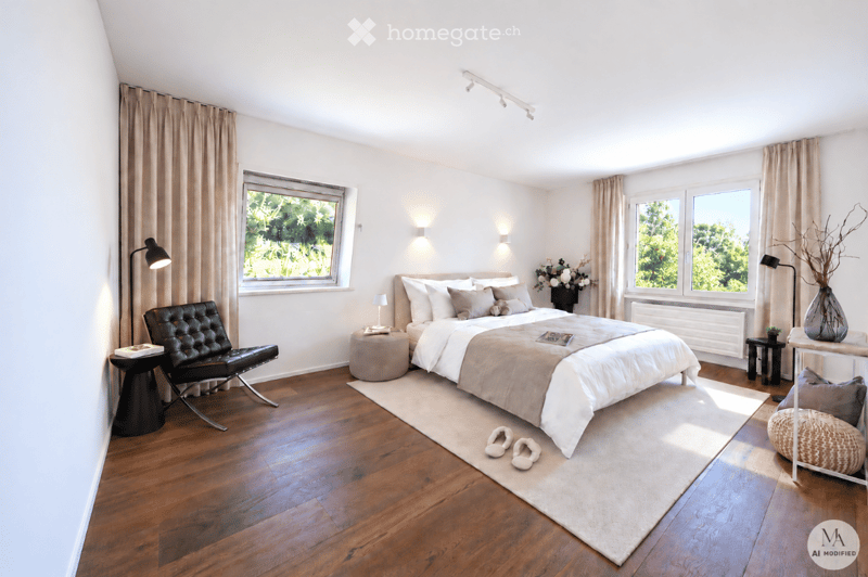 Modern bedroom with wooden flooring, large windows, a bed with white and beige bedding, a black leather chair, a small table, and decorative vases.