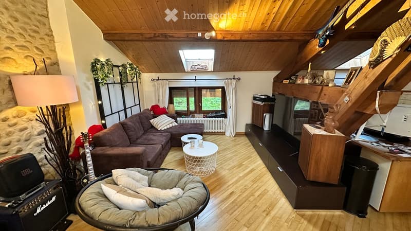 Cozy living room with wooden ceiling beams, exposed stone wall, large window with curtains, sofa, coffee table, dog bed, guitar, and floor lamp.
