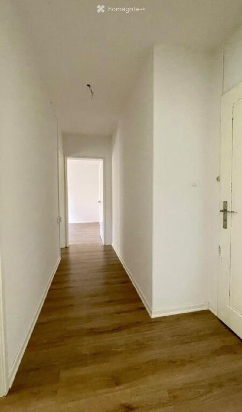 Empty hallway with wooden flooring and white walls, featuring a single door at the end.