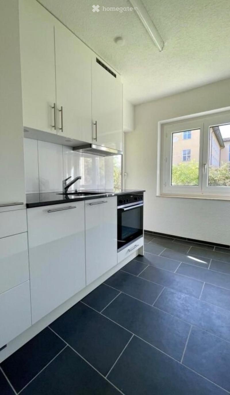 Modern kitchen with white cabinets, dark tiled floor, and stainless steel appliances including a sink and oven.