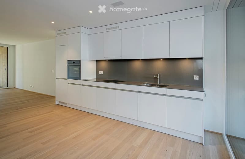 Modern kitchen with white cabinets, stainless steel appliances, and wooden flooring.