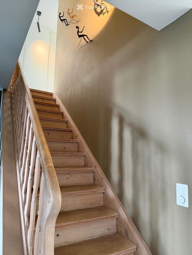 Wooden staircase with a curved handrail and light-colored walls, featuring decorative shadow figures on the wall.