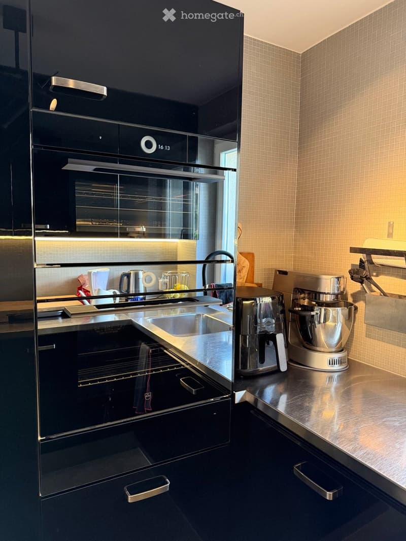 Modern kitchen with stainless steel appliances, including an oven, sink, and mixer, along with a countertop and various small items.