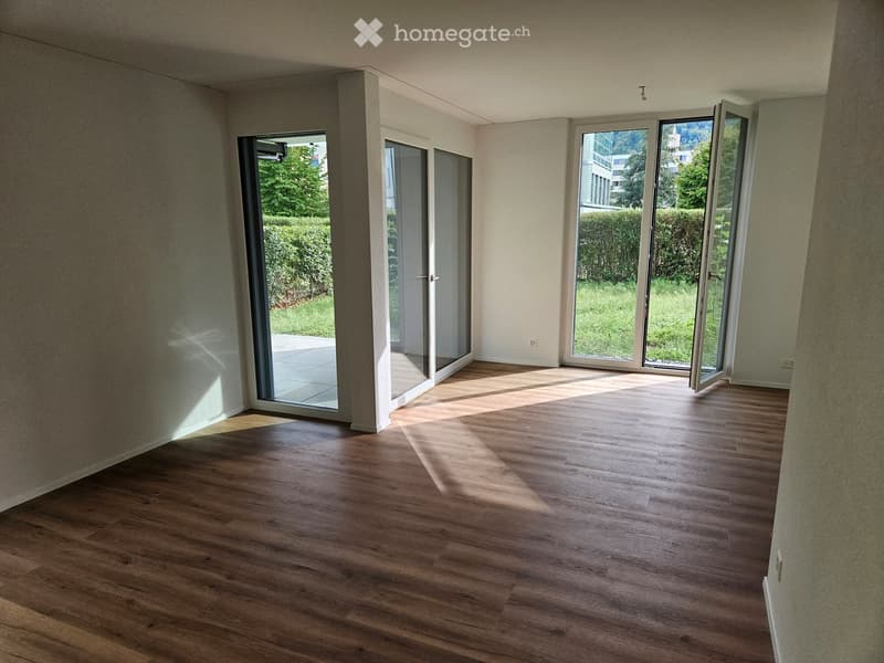 Empty room with wooden flooring and large sliding glass doors leading to a garden area.