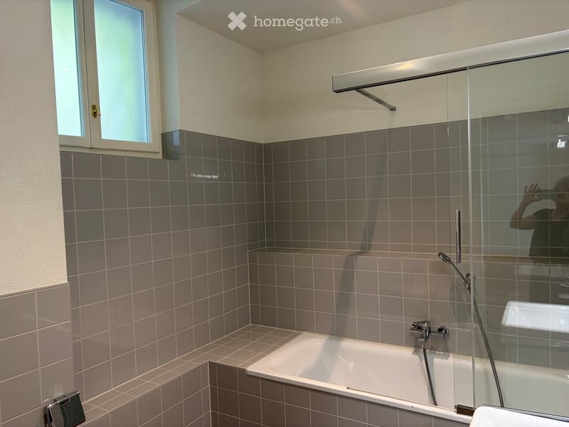 Modern bathroom with a bathtub, glass shower enclosure, tiled walls, and a window for natural light.