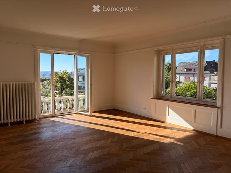Empty room with wooden herringbone flooring, large windows, and a sliding glass door leading to a balcony.