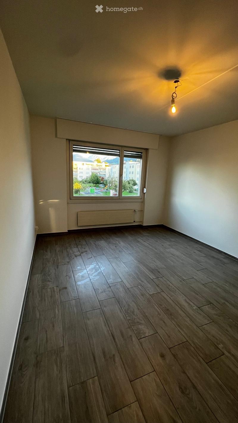 Empty room with wooden flooring, white walls, and a large window offering a view of the outside area.