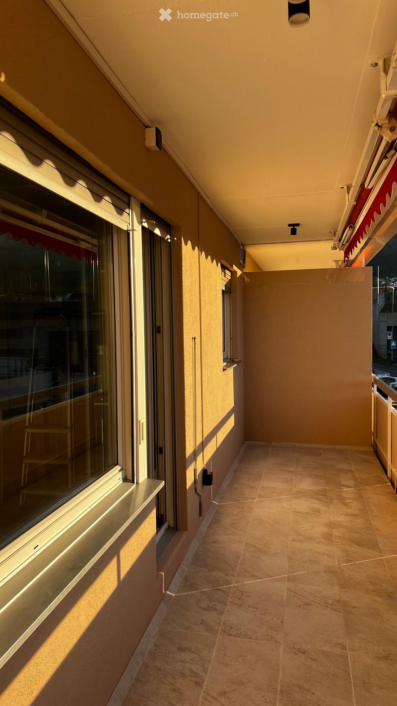 Balcony with tiled floor, beige walls, large windows, and a covered section with a red awning.