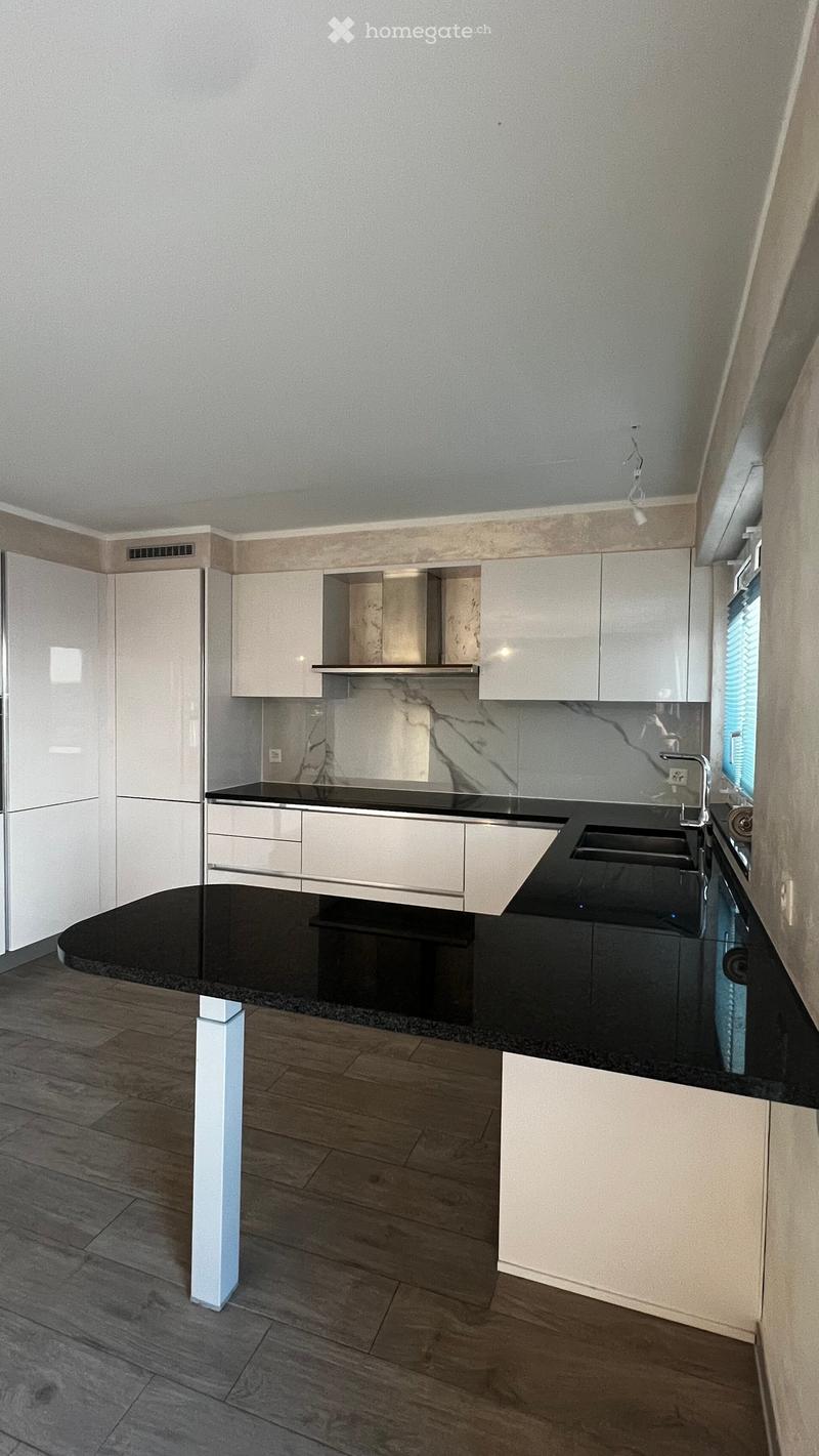 Modern kitchen with white cabinets, black countertops, and a sleek design. Features a central island with a sink and faucet, and a marble backsplash.