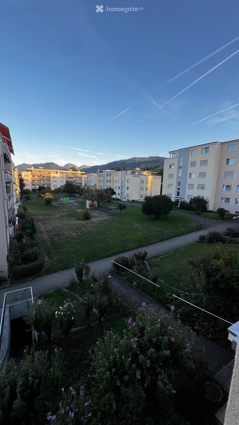 View of a residential area with green spaces, pathways, and buildings in the background.