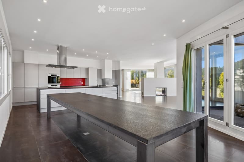 Modern kitchen with white cabinets, stainless steel appliances, a large central island, and a fireplace in the background.