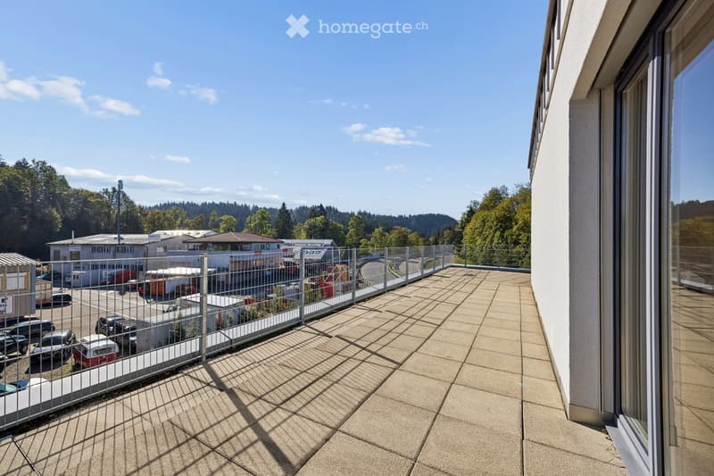 Balcony with tiled floor, metal railing, and view of a parking lot and surrounding greenery.