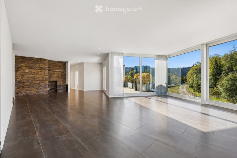 An empty, modern living space with large glass sliding doors leading to an outdoor area, polished dark tile flooring, and a textured stone accent wall.