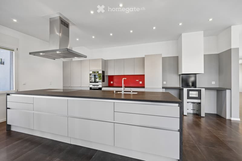 Modern kitchen with white cabinets, dark countertops, a central island, and a stainless steel range hood.