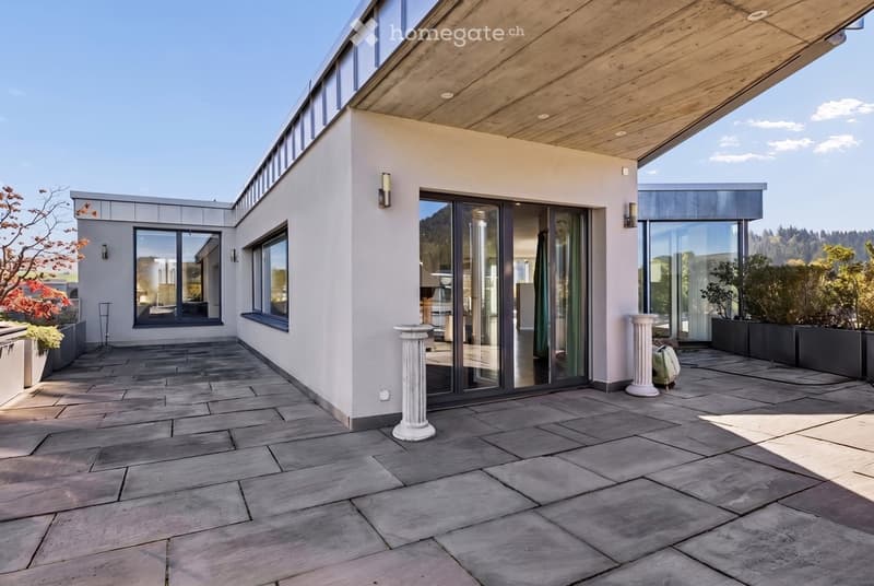 Modern outdoor terrace with stone tiles, white columns, large glass sliding doors, and surrounding greenery.