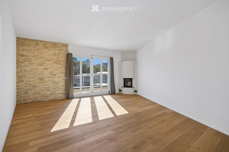 Empty room with wooden flooring, white walls, a stone accent wall, large glass doors leading outside, and a built-in fireplace.