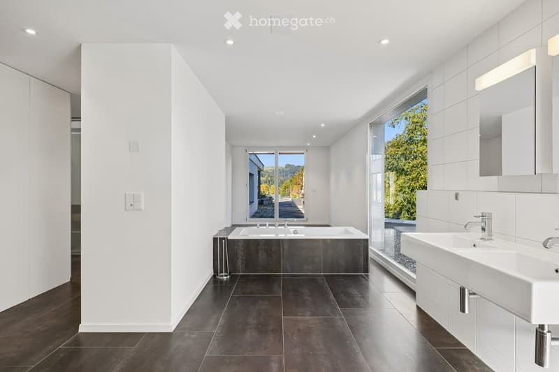 Modern bathroom with dark tiled floor, white walls, large windows, bathtub, sink, and mirror.