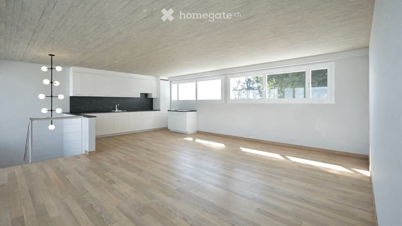 Modern kitchen with white cabinets, a central island, and a sleek black countertop. The space features wooden flooring and large windows allowing natural light to fill the room.