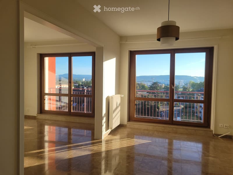 Empty room with large windows, tiled floor, radiator, and a view of the city and mountains.
