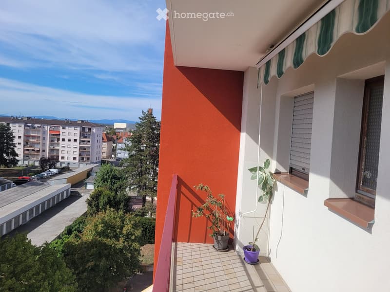 Balcony with tiled floor, potted plants, and a view of a residential area with buildings and trees.