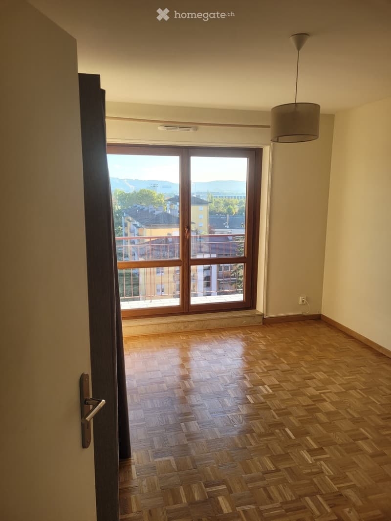Empty room with wooden herringbone flooring, large sliding glass door leading to a balcony, and a hanging pendant light fixture.