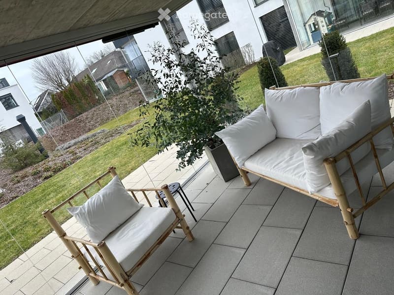 Balcony with a sofa, chair, small table, and potted plant, overlooking a well-maintained garden.
