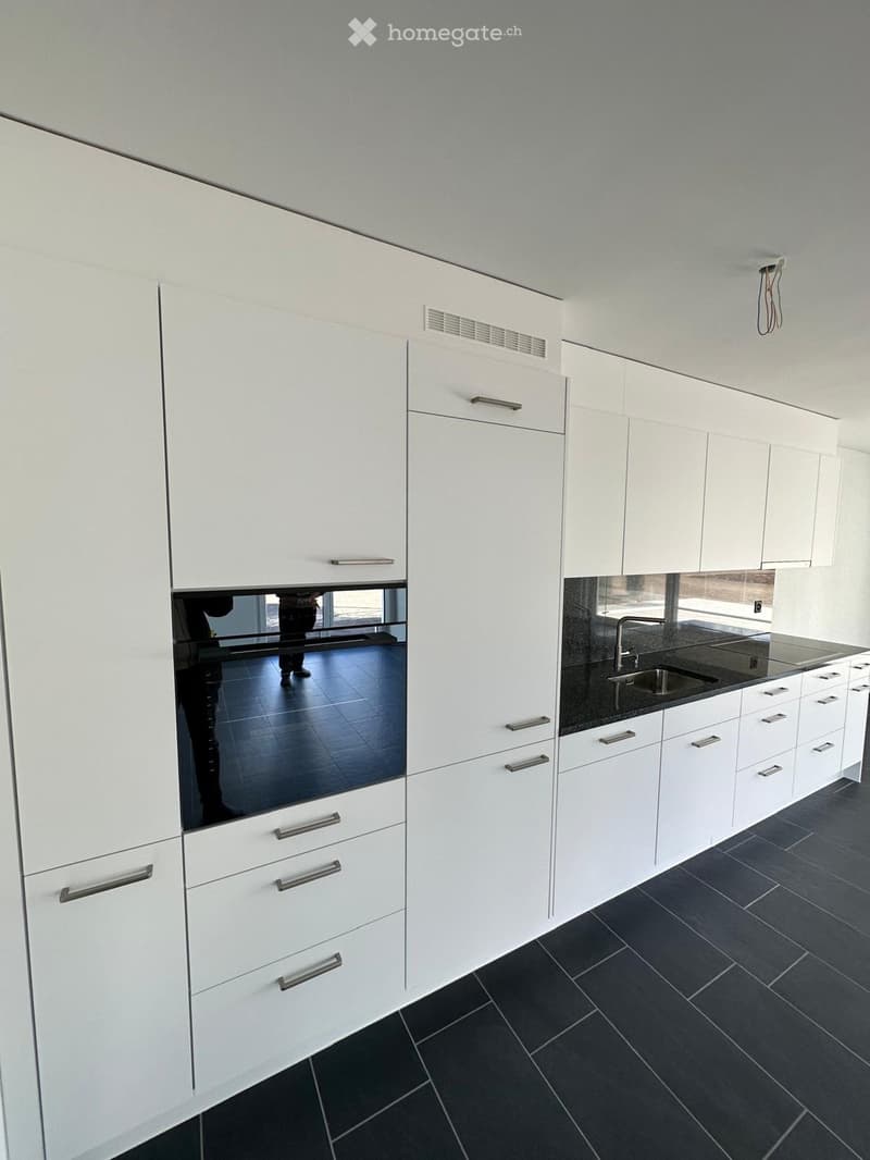 Modern kitchen with white cabinets, dark tiled floor, and stainless steel sink.