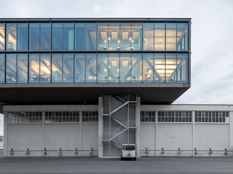 modern design building with glass exterior, large windows, steel staircase, metal railings, large white walls, charging points with bicycles, white van parked