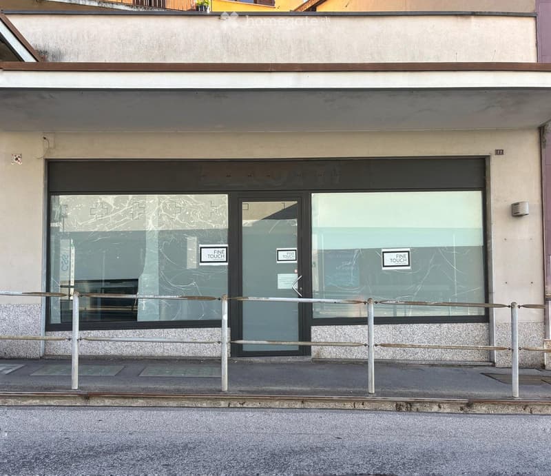Facade of a commercial building with large glass windows and a central entrance door, featuring a metal barrier in front.