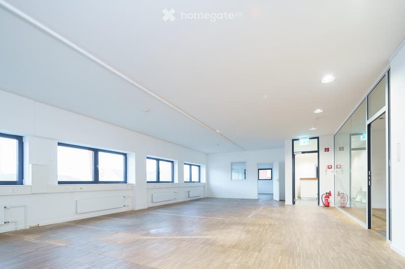 Empty room with white walls, wooden flooring, large windows, and a glass door leading to a hallway.