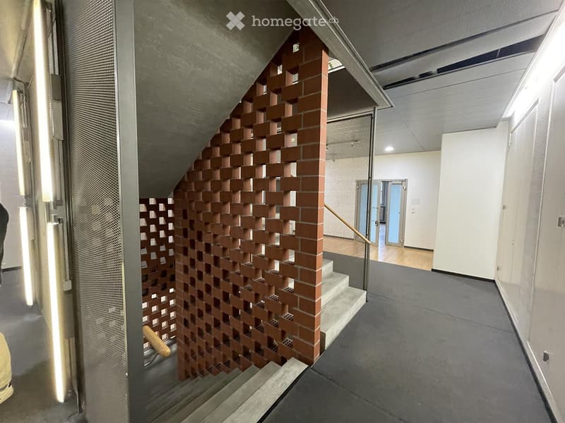Modern hallway with a staircase, brick wall design, and glass doors leading to another room.