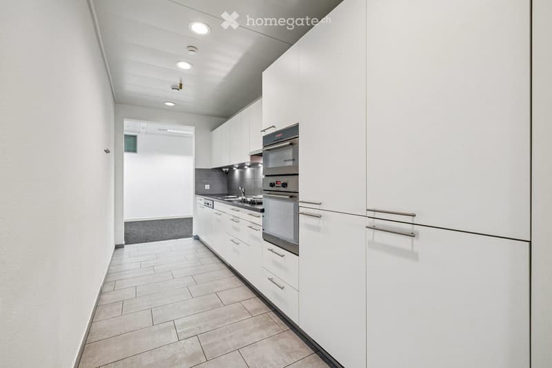 Modern kitchen with white cabinets, stainless steel oven, sink, and faucet. Light-colored tiled floor and walls.