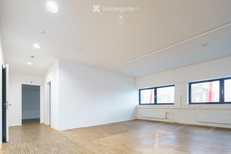 Empty room with light-colored walls, wooden flooring, and large windows. No furniture or equipment is present.