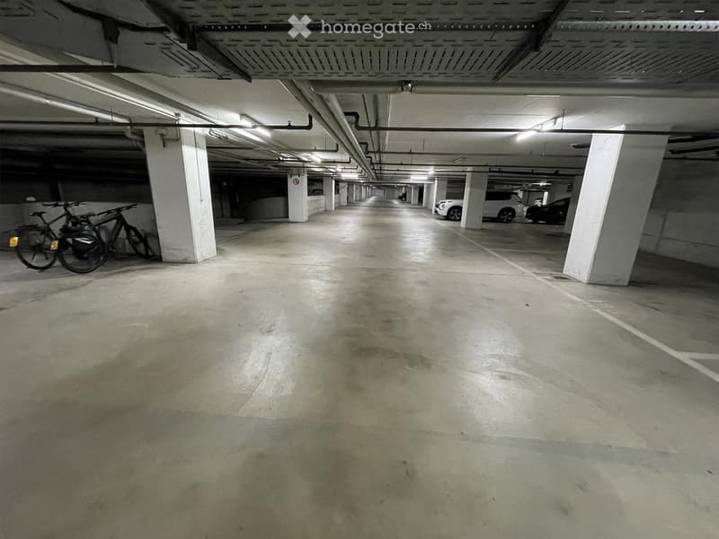 Underground parking area with concrete floors, white pillars, and a few parked cars and bicycles.