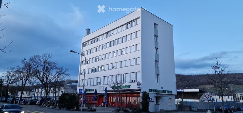 Building. A modern, multi-story white building with a restaurant on the ground floor, featuring large windows and a clean facade.