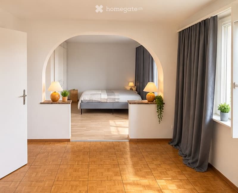 Bright, modern bedroom with wooden flooring, arched doorway, and minimalist decor including a bed, nightstands, table lamps, and small potted plants.