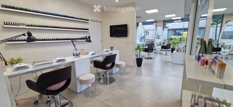 Modern, well-lit salon with white furniture, multiple chairs, mirrors, and shelves filled with nail polish bottles.