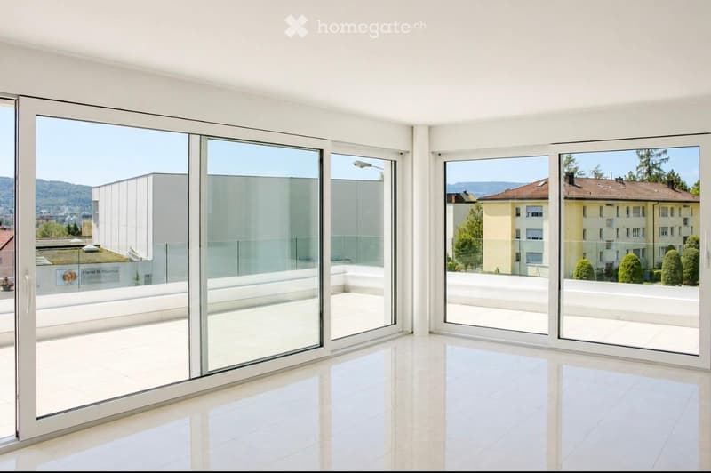Bright, empty room with large glass sliding doors opening to a balcony, offering a scenic view of buildings and greenery.