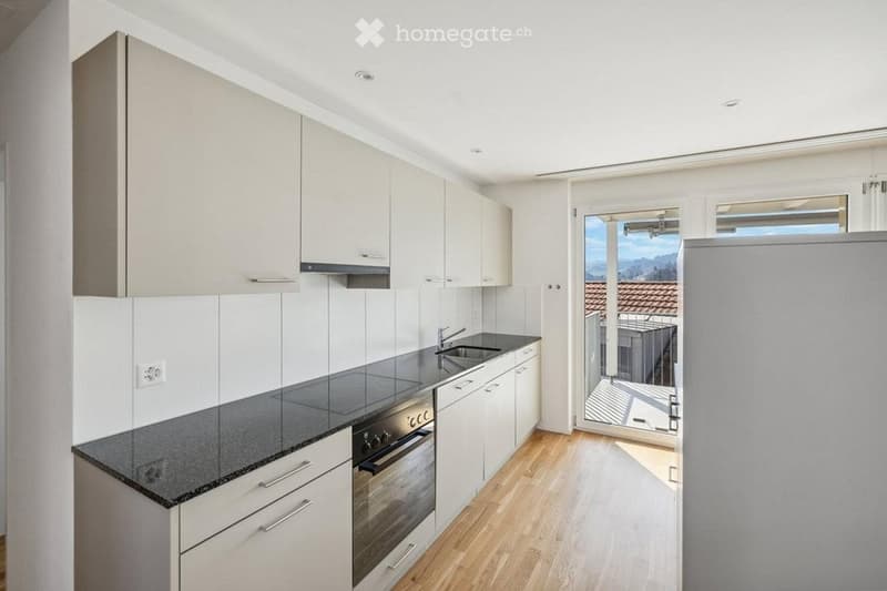 Modern kitchen with white cabinets, black countertop, stainless steel sink, and built-in oven. Features a large window and a sliding glass door leading to a balcony.