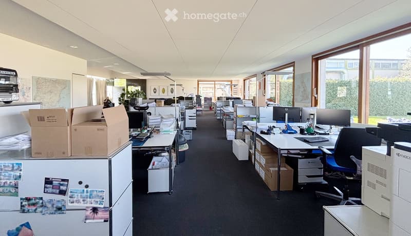 Office space with desks, chairs, computers, storage boxes, and large windows